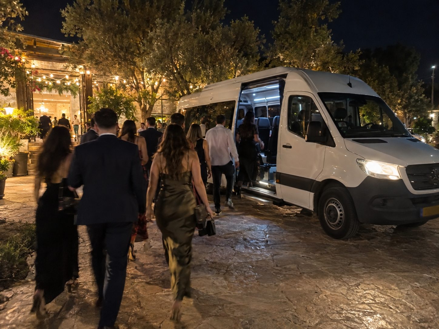 Wedding guests boarding a white minibus shuttle outside an evening celebration